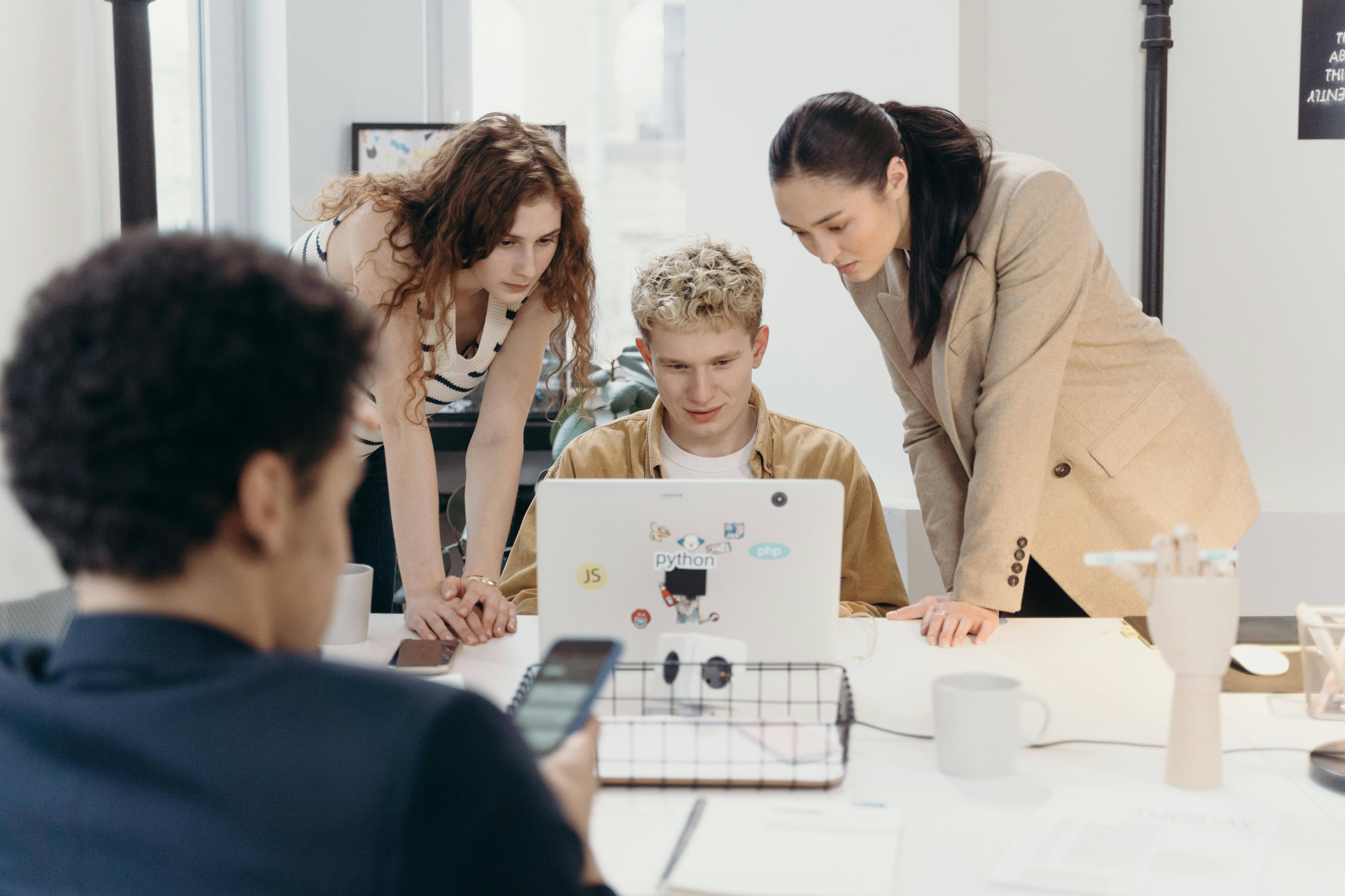 women-standing-beside-a-man-using-a-laptop